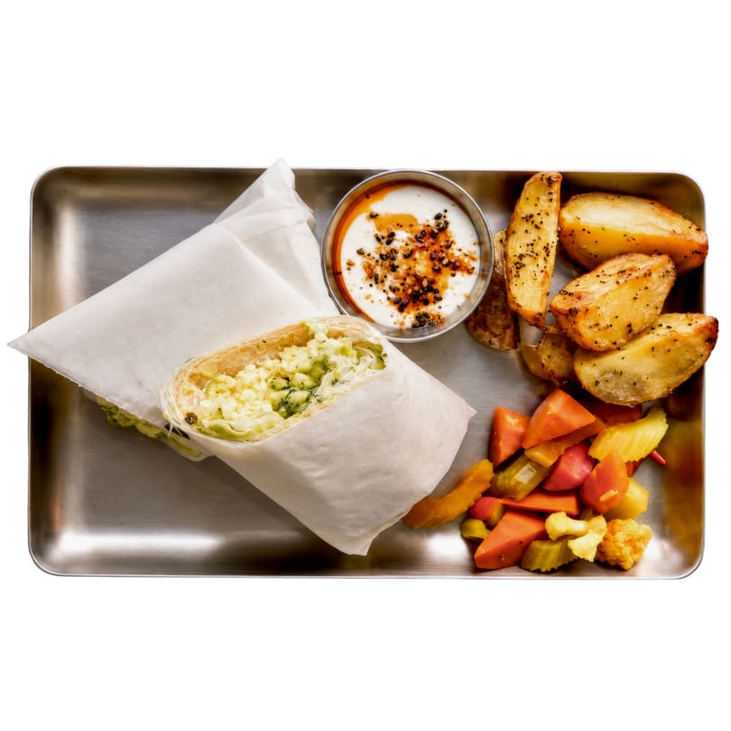 A wrap with scrambled eggs and avocado, served with roasted potatoes, pickles, and yogurt sauce.