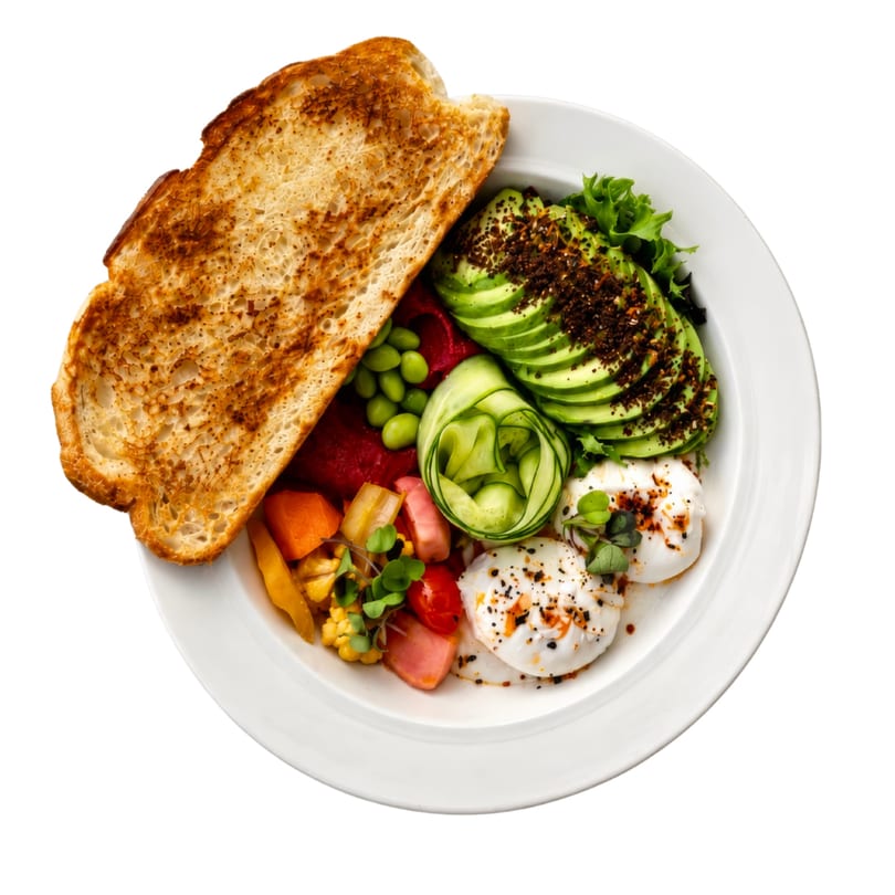 A vibrant breakfast bowl with avocado, poached eggs, vegetables, and toast on a white plate.